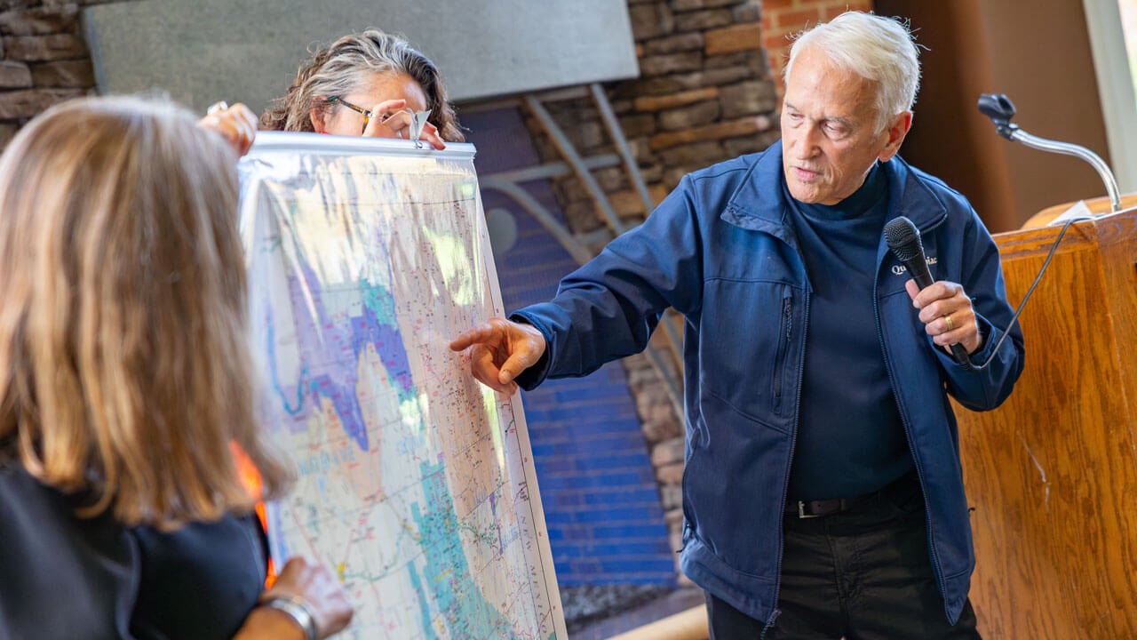 Presenter pointing to a map while speaking into a microphone at the indigeneity initiative teach in