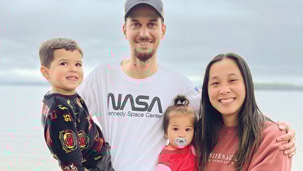 Emily Van Fleet and her husband hold their two children with a beach in the background