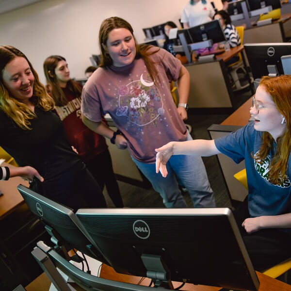 2 female QU students look at a young girl who is coding on a computer