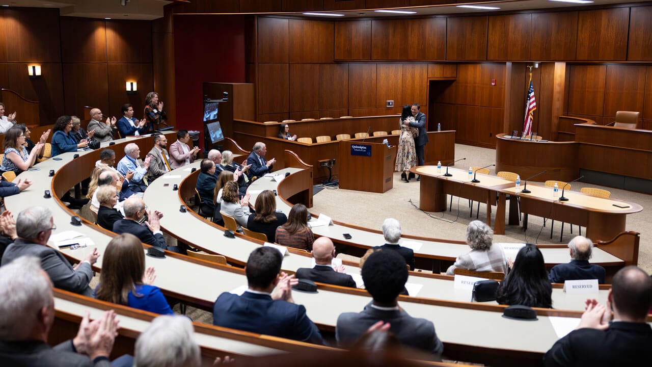 A wide shot of the entire audience at the inaugural alumni association awards and two people hugging at the front of the room.