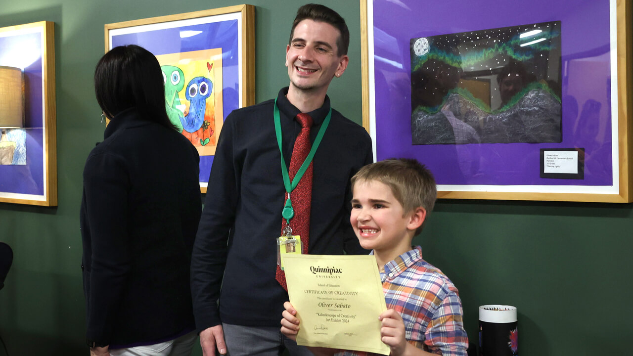 A young boy standing in front of his artwork with his teacher