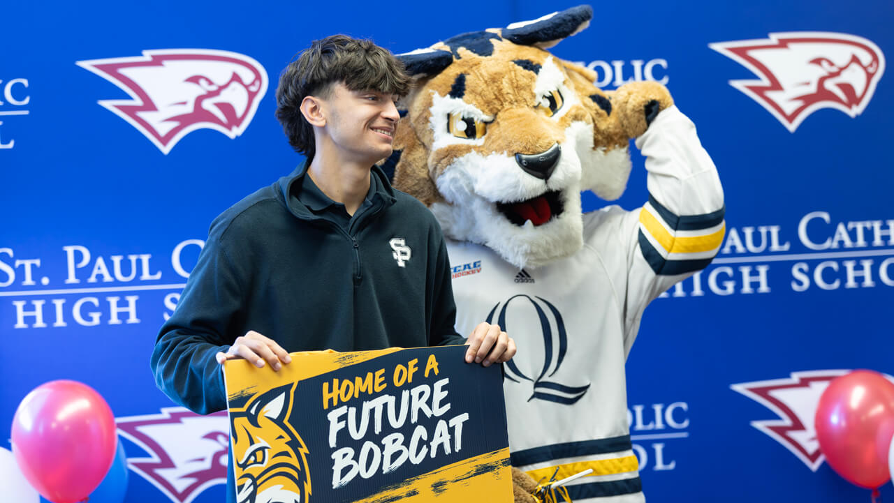 A new student holds a "Home of a Future Bobcat" sign with Boomer the mascot