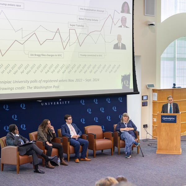 A panel of faculty and staff in the Mount Carmel Auditorium with a projected slide of an election data graph