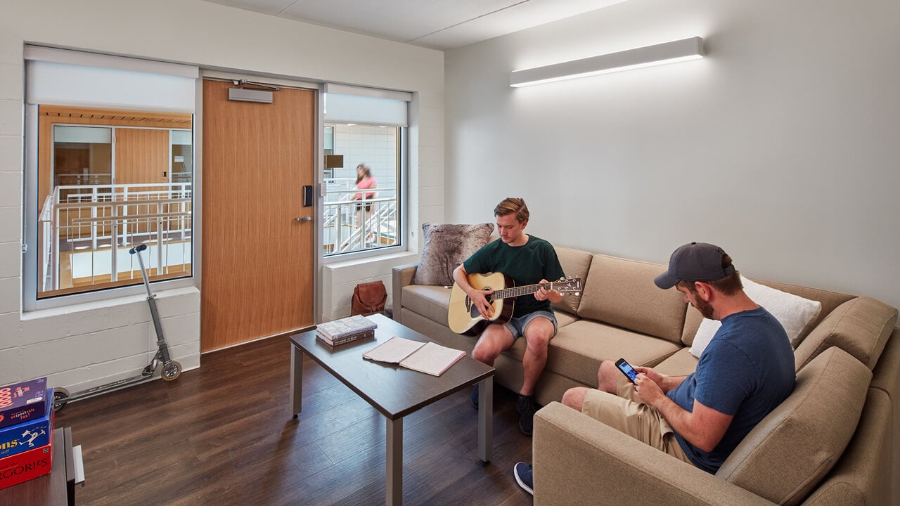 Two roommates hang out in their common room looking out onto the second floor of the atrium