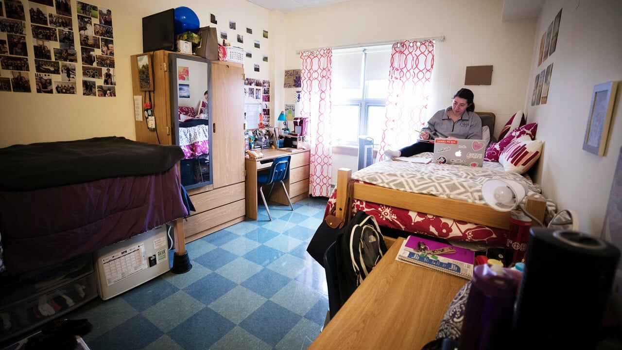 A student sits on her bed with a laptop