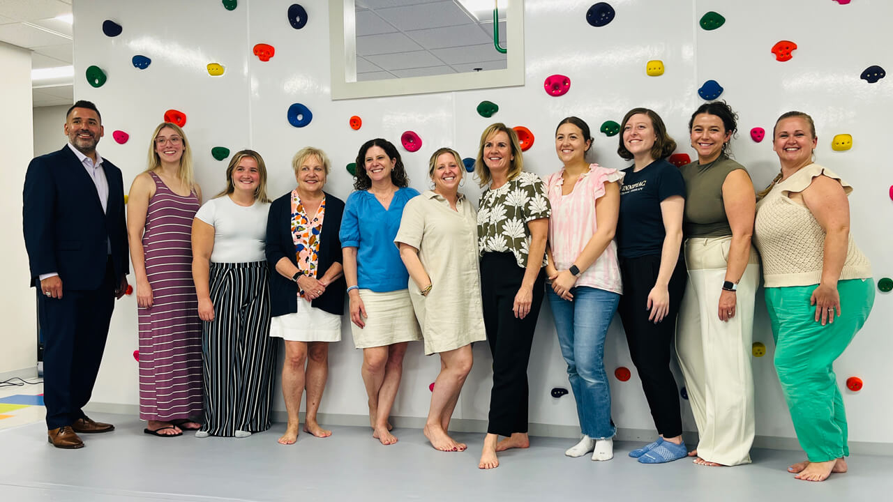 A group of Quinnipiac occupational therapy alumni pose for a photo in front of a colorful climbing wall