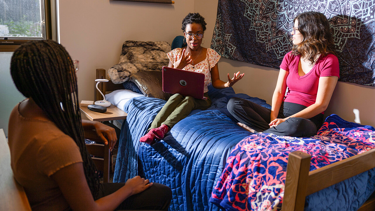 Three girls sit on a bed in The Grove residence hall