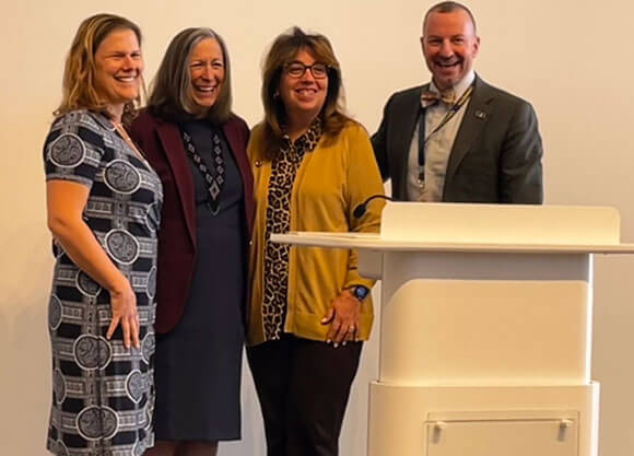 Four individuals smile at a podium