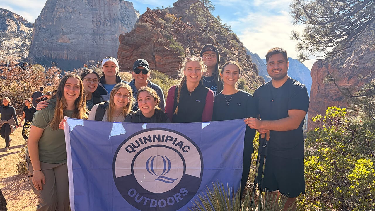 Students hold Quinnipiac Outdoors flag in Utah