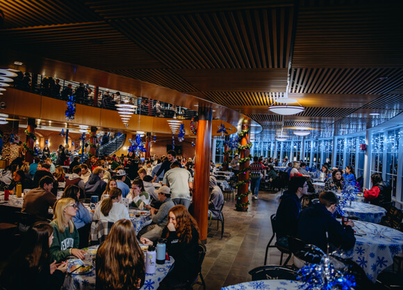 Dozens of students enjoy a meal together in the dining hall decorated with holiday decorations