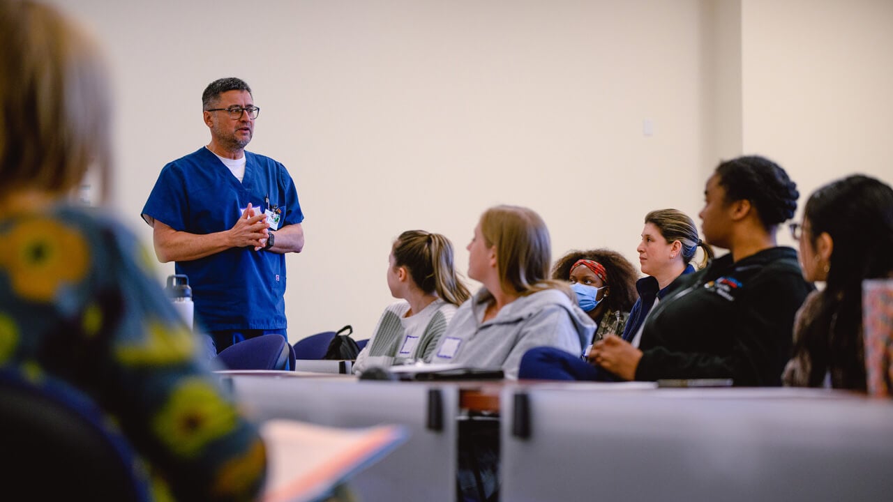 A man in scrubs standing in front of a seated group, speaking