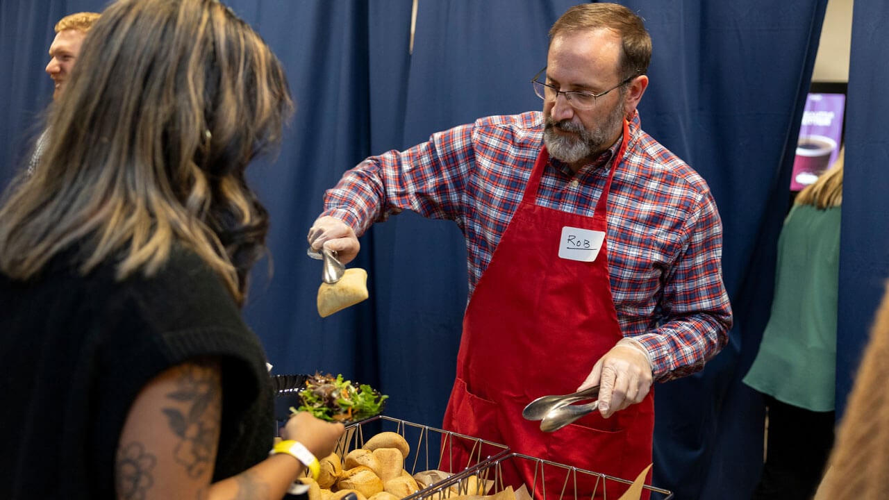 Professor serves student a bread roll in the North Haven Cafe