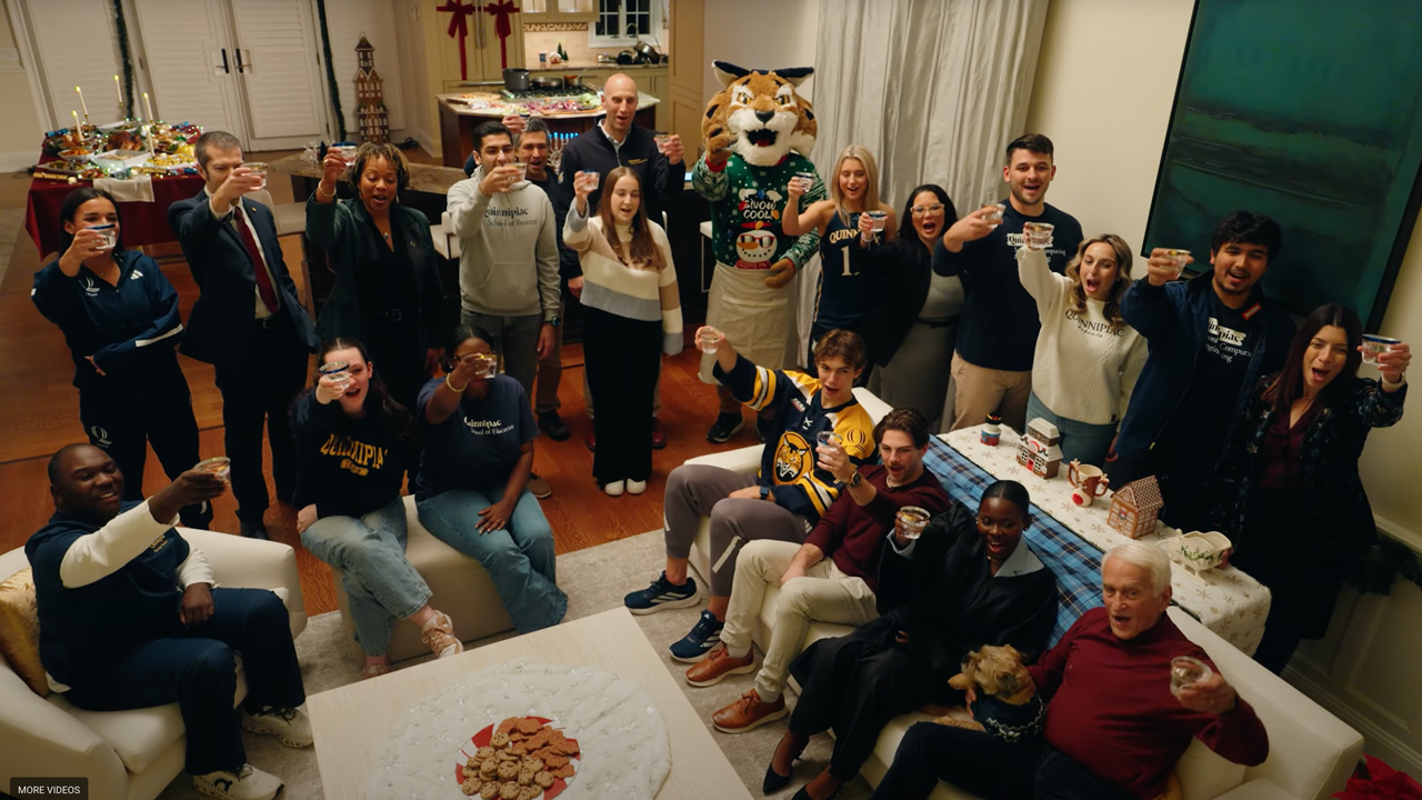 Dozens of Quinnipiac students, faculty and Boomer hold up glasses in cheers