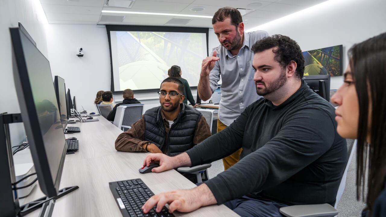 Professor speaking to group of students working on a PC