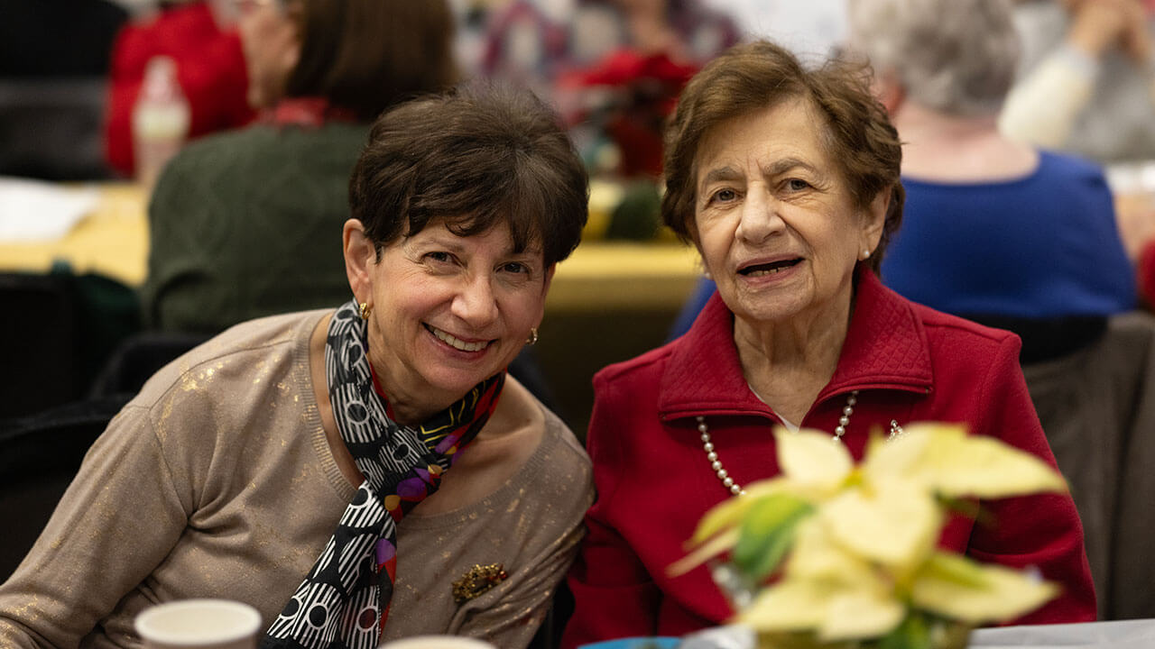 Two women smile while wearing their Christmas sweaters.