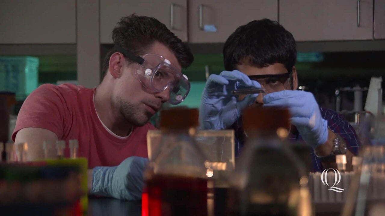 Two students carefully measure liquids using test tubes and beakers in a lab classroom