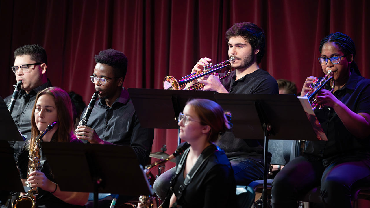 Saxophone and trumpet players sit in seats and play their instruments during their winter concert.