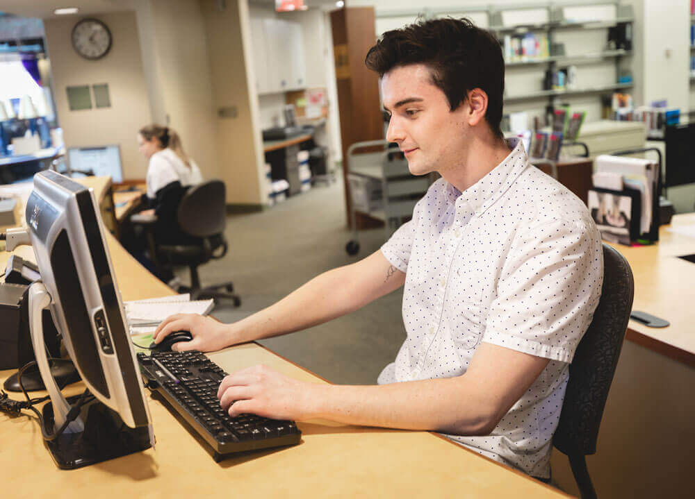 Students works on a computer at the reference center in the Arnold Bernhard Library