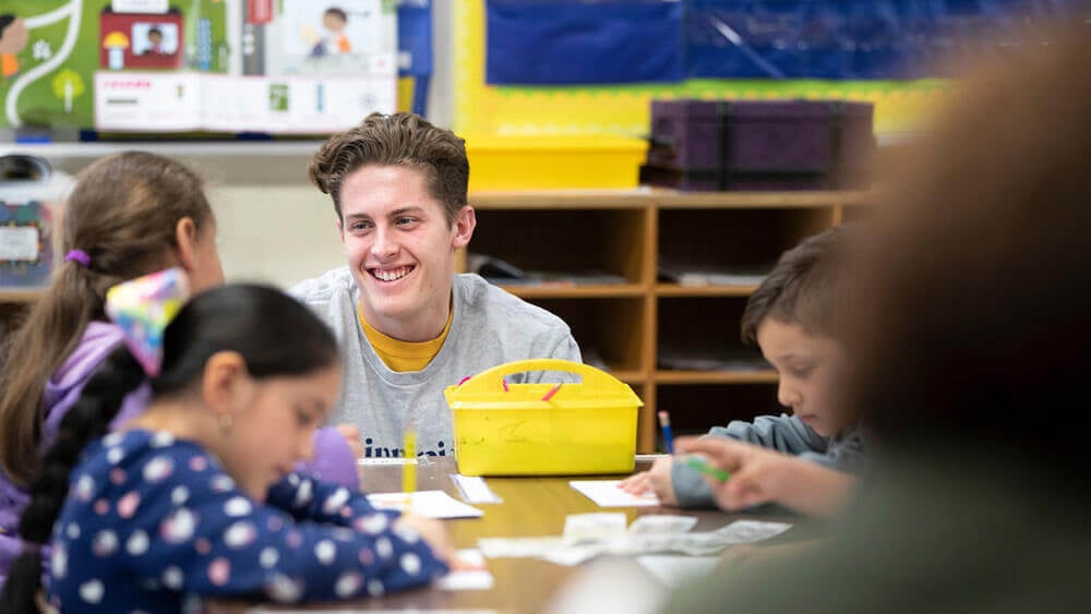 A business student crouches down to talk to an elementary schooler