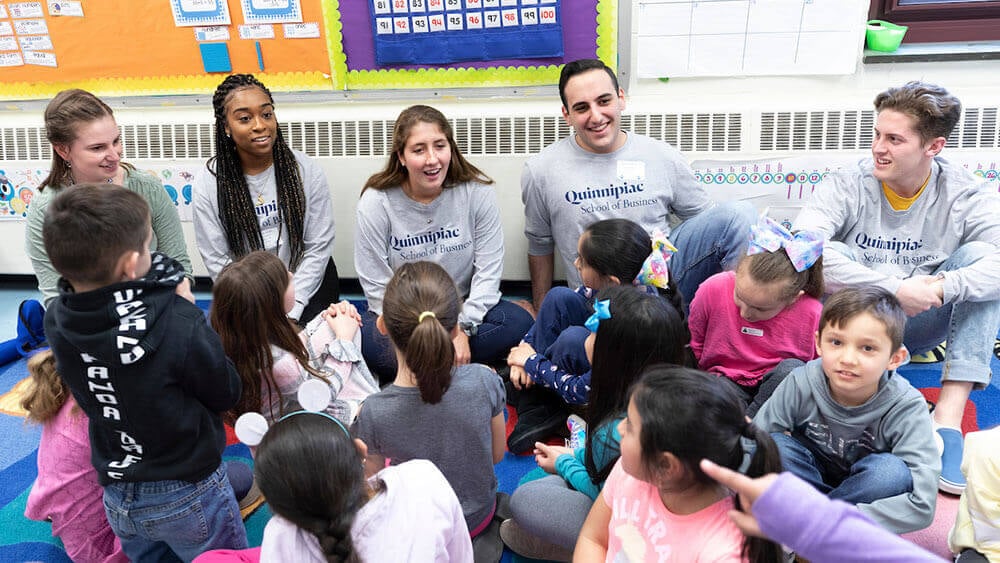 Business students sit down in a circle among elementary schoolers