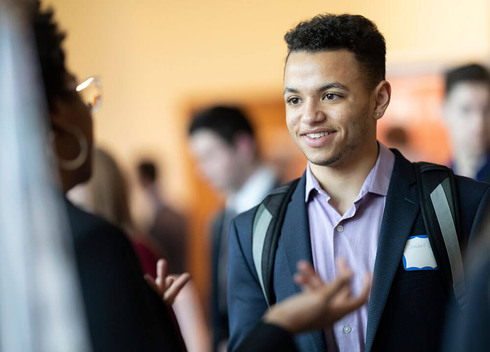 A communications student dressed in a suit interviews with a potential employer at a career fair