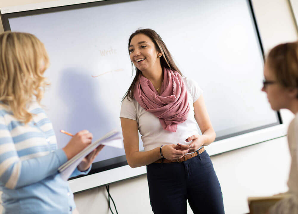 Three School of Education students talk with one another about a project in front of a white board