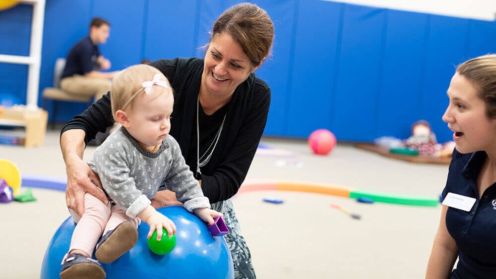 A professor holds a baby sitting on top of an exercise ball