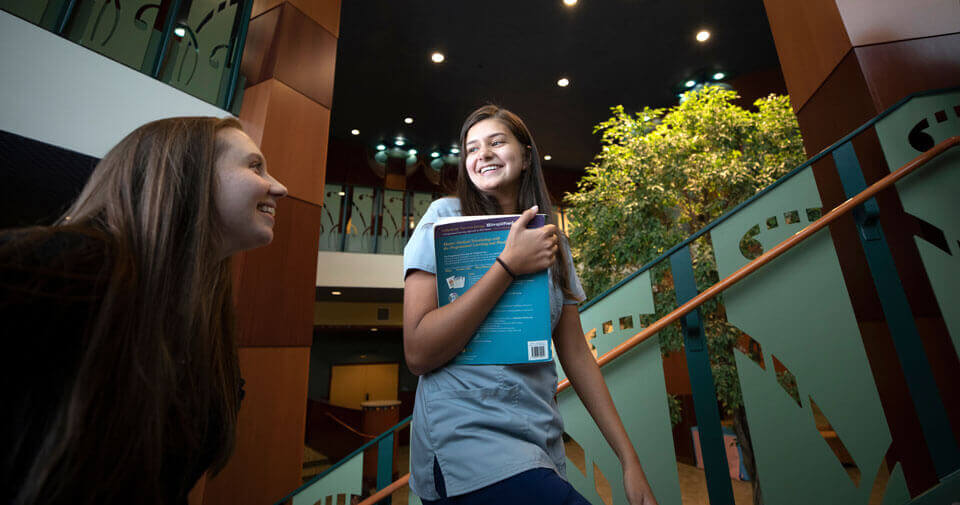 Two graduate students walk up the atrium stairs on the Quinnipiac North Haven Campus