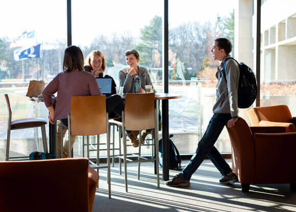 Graduate students laugh and talk together in front of large bright windows