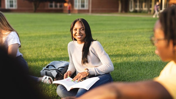 Two students sit and talk on the lawn of the quad