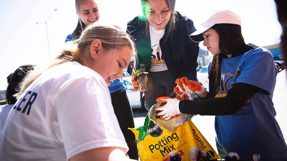 Four students gather around a bag of potting soil as they plant flowers at a local library