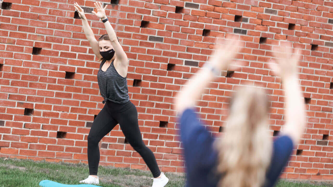 A student wearing a mask performs yoga poses in the grass