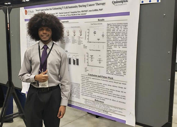 Andrew Depass stands in front of a bulletin board displaying information about his research project.