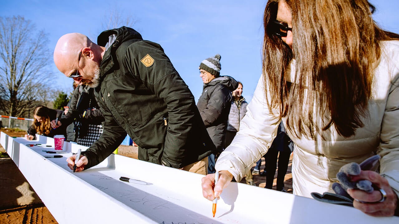 Two QU staff members sign the beam for one of the buildings on the South Quad.