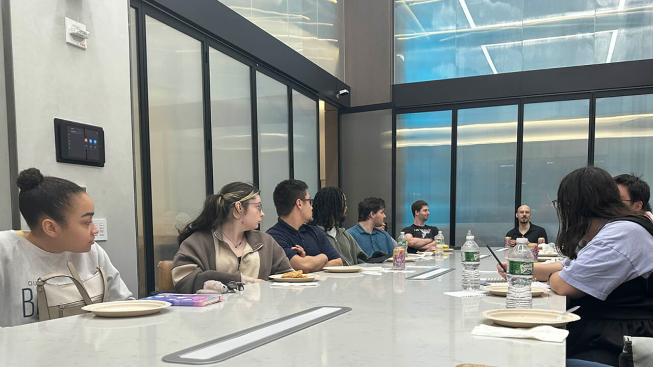 A group of students sitting at a conference table, listening to a man speak while sitting at the head of the table