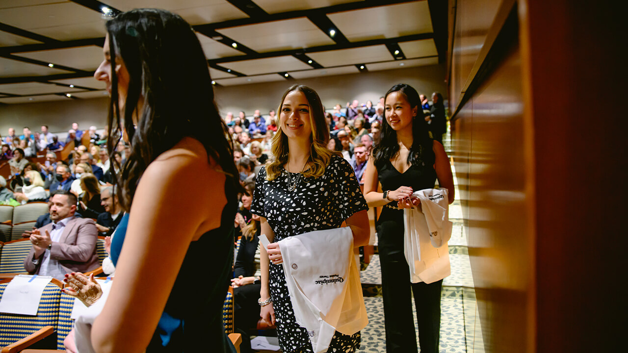 Students walking in with their white coats, smiling at the camera.