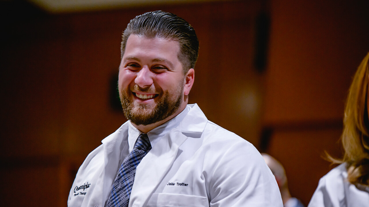 A student with their white coat on smiles at the camera.