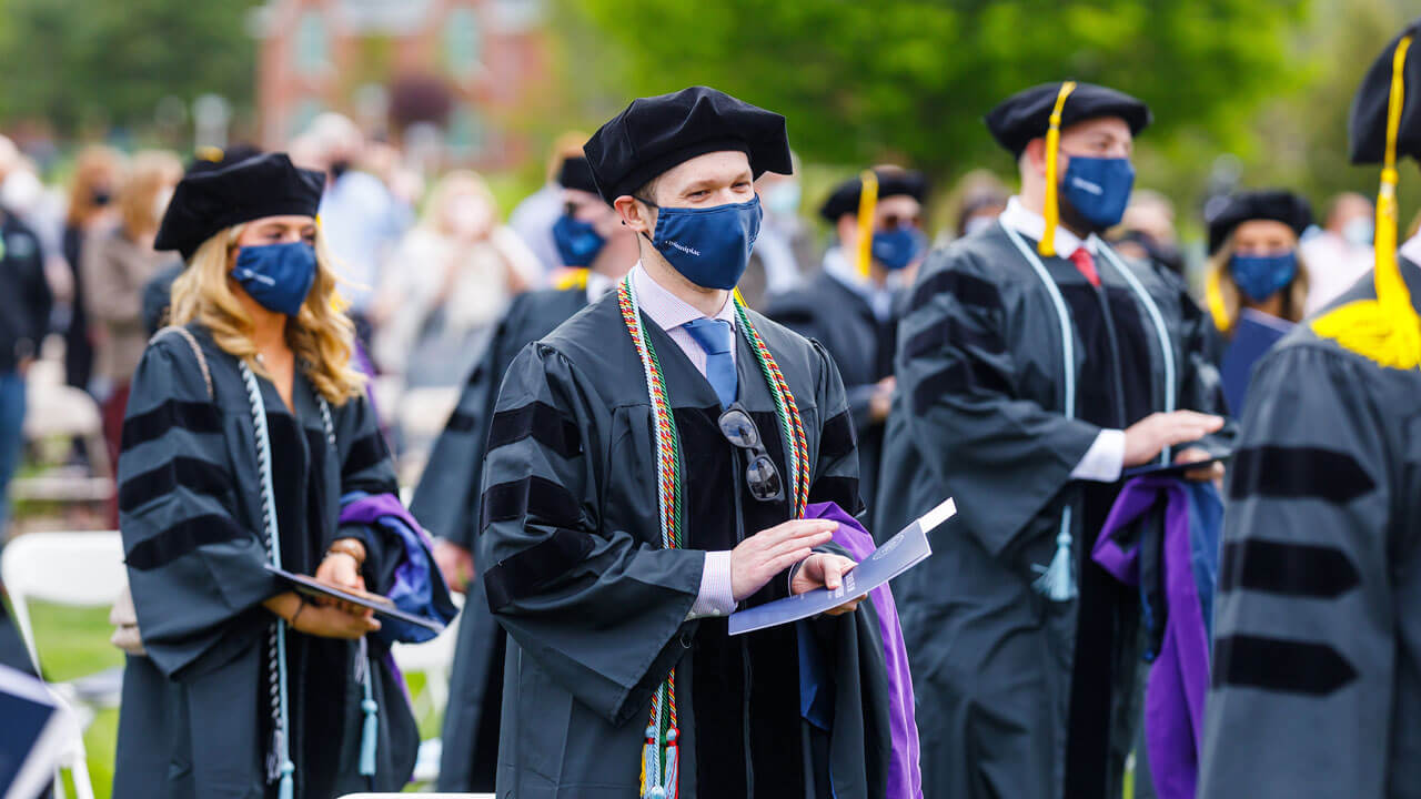 Graduates clap their hands as they stand on the quad