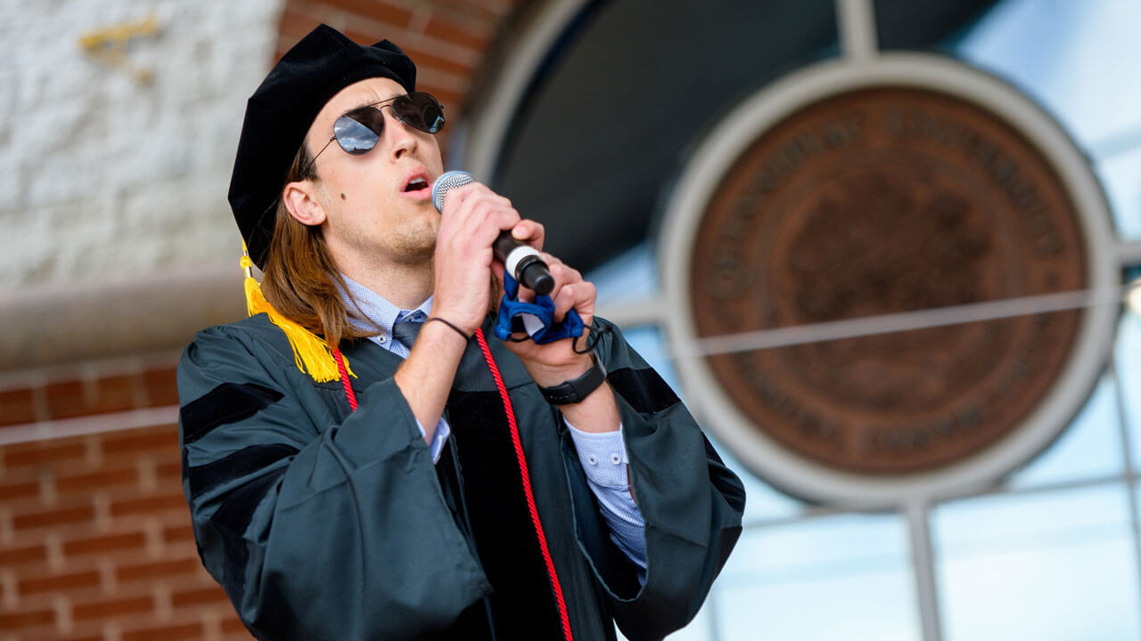 Alexander Puzone sings with a microphone on the library steps