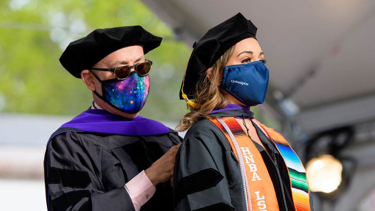 A graduate recieves her doctoral hood from a faculty member