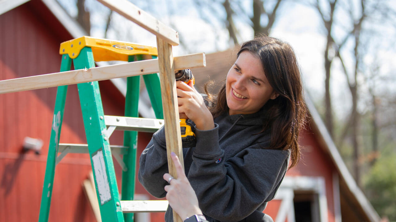 Girl up on ladder drills into pieces of wood while building outside at the Big Event