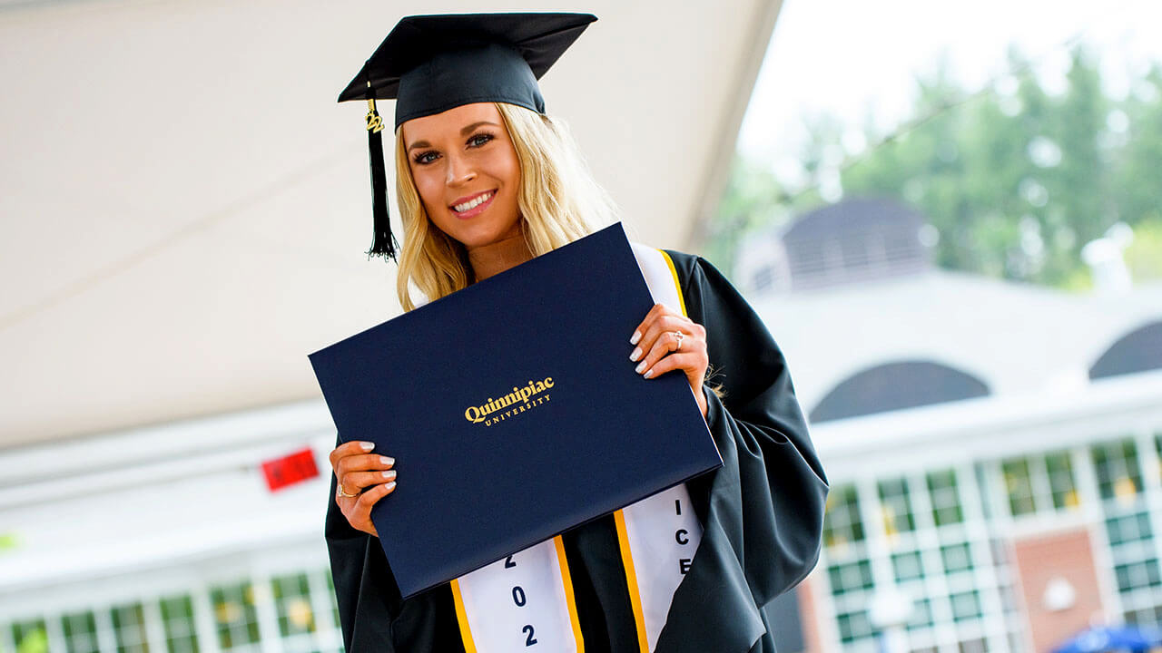 A graduate holds up their diploma on stage