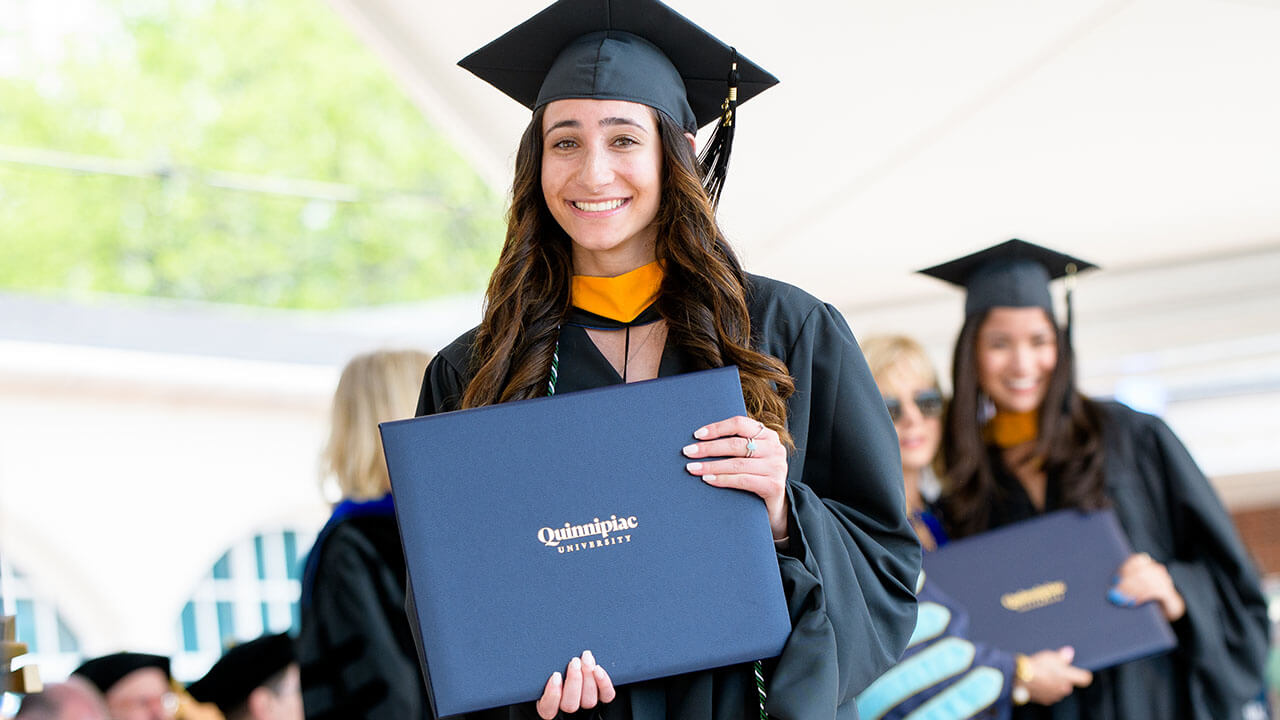 Graduate holds up their diploma and smiles on stage