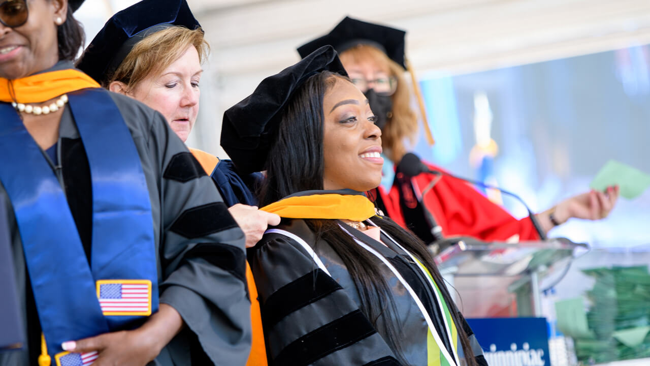 A graduate being hooded on stage at Commencement.