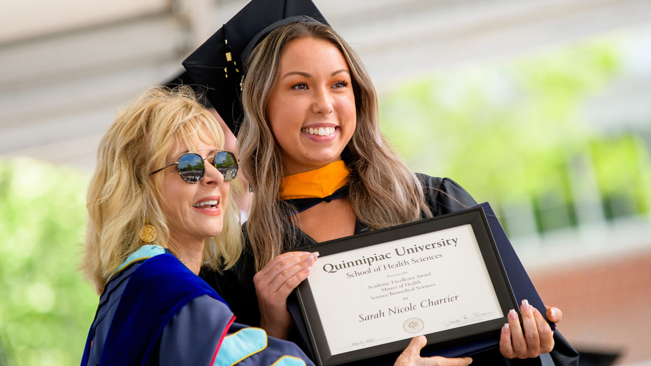 President Olian poses for a photo with a graduate after handing her a diploma