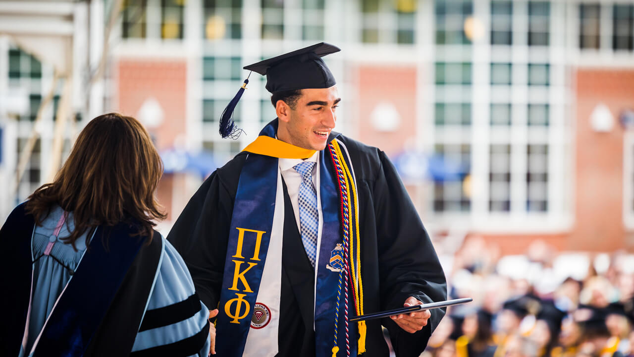 A graduate shakes hands with a faculty member on stage