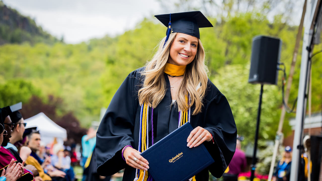 A graduate smiles as she walks back to her seat with her diploma cover