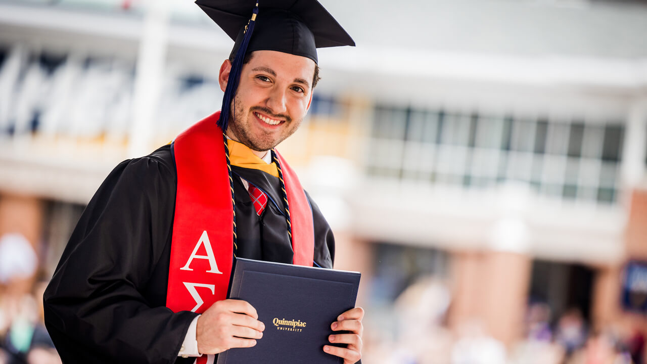 A graduate holds up his diploma cover as he smiles