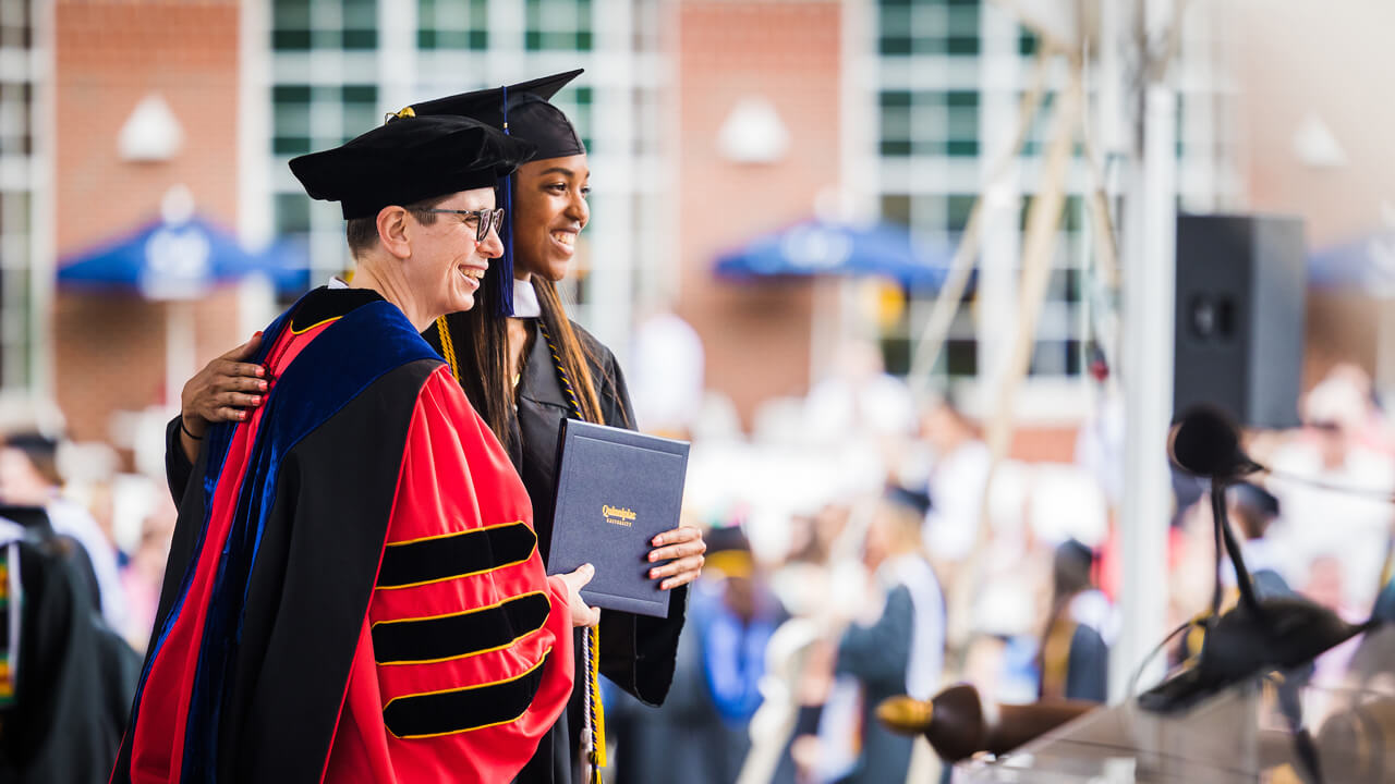 A graduate poses for a photo with Provost Debra Liebowitz