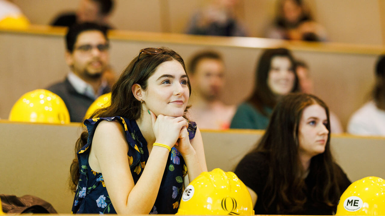 girl leaning elbows on table looking up at presentation during hard hat ceremony